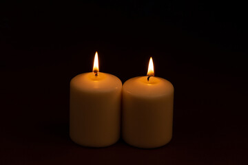 Fototapeta na wymiar Two white candles flame burning on dark background with copy space for text.