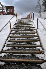 Wooden mountain trail in winter. Stairs with wooden railing in the mountains. Landscape with mountain path. Trail leading to the mountain peak. Adventure and travel.