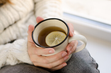 Young woman on the windowsill with a cup of tea. A cup of tea with lemon in female hands.