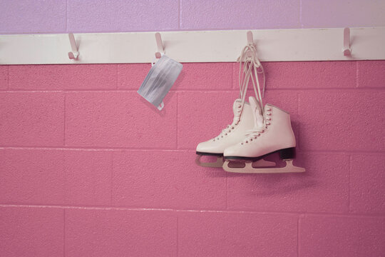 Girly figure skates with a surgical mask, hanging in pastel background with copy space. COVID 19