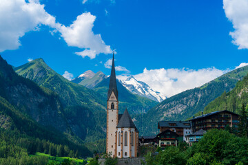 Fototapeta na wymiar A scenic landscape photo of the Austrian municipality of Heiligenblut with St. Vincent Church in front of the Hohe Tauern mountains. Cetral Alps mountains in the background.
