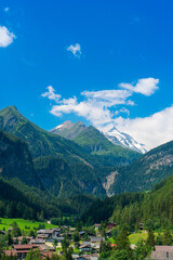 A scenic landscape photo of the Austrian municipality of Heiligenblut with St. Vincent Church in front of the Hohe Tauern mountains. Cetral Alps mountains in the background.