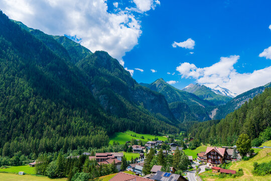 A scenic landscape photo of the Austrian municipality of Heiligenblut with St. Vincent Church in front of the Hohe Tauern mountains. Cetral Alps mountains in the background.