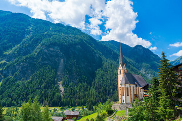 Fototapeta na wymiar A scenic landscape photo of the Austrian municipality of Heiligenblut with St. Vincent Church in front of the Hohe Tauern mountains. Cetral Alps mountains in the background.