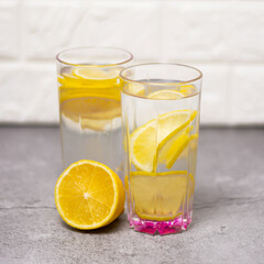 Purified water with lemon in a transparent glass with a pink bottom on a brick wall background. A healthy way of life. Square photography.