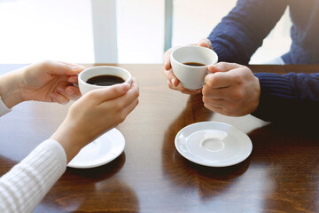 Female and man hands with cups of coffee on the background of a wooden table