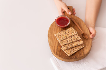 The girl is holding a wooden board with organic whole grain crispy chips with strawberry jam in her hands on the kitchen table. Healthy food and nutrition.