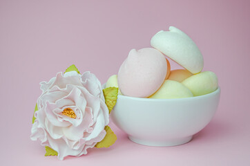 Meringues in a white Cup and a flower on a pink background.