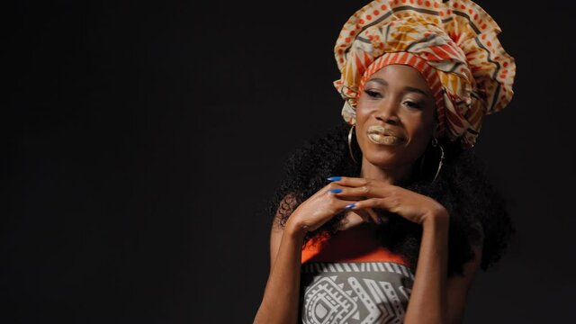 Traditional headdress beautiful Afro American young woman dancing and smile looking at camera sideways isolated on black background. High quality 4k resolution footage. 