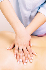 Massage therapist hands massaging client's back close-up in beauty salon