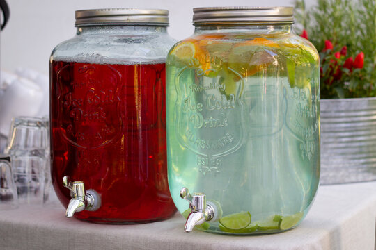 Selection of refreshing ice cold lemonade drinks in large tap glass jars. Healthy catering service buffet table at a summer party.