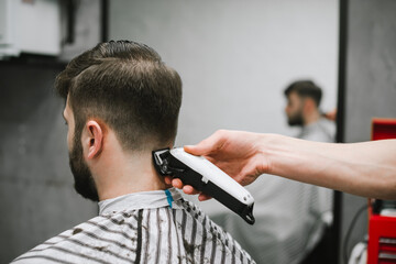 Close photo. Hairdresser's hand with clipper cuts hair of bearded adult man, back view. Barber job concept. Creating a stylish men's hairstyle. Copy space