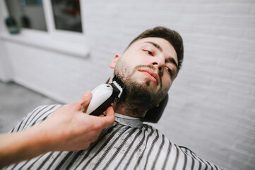 Closeup photo of a barber cutting a hair of an adult man on a beard. A male hairdresser creates a beard hairstyle for a handsome bearded man. Barber shop services.