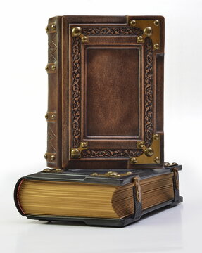 Closed brown leather book with ornate frame and metal corners stand up over the black book