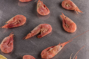 shrimps on a gray stone table with lemons, salt and herbs and ice cubes