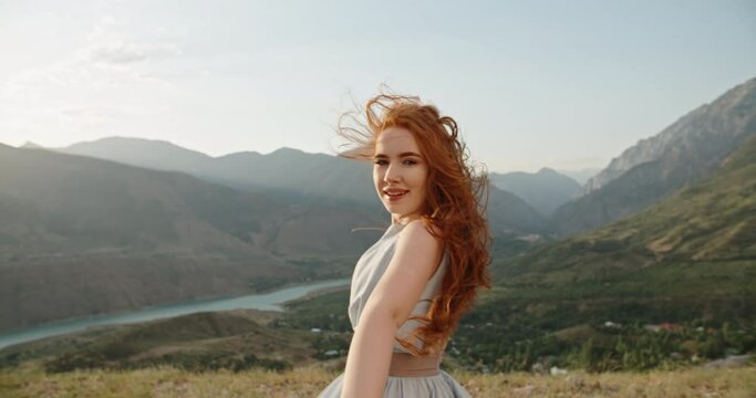 Beautiful caucasian girl wearing white dress on top of a mountain. Gorgeous woman looking at camera and positively smiling 4k footage