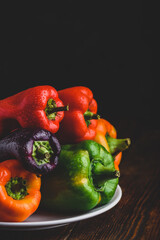 Multicolored fresh bell peppers on plate over wooden background