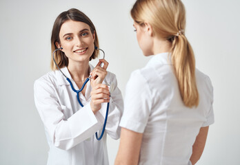 doctor with a stethoscope examines a woman in a white t-shirt on a light background 