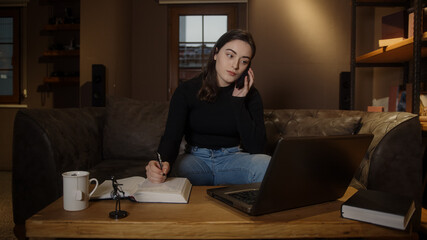 Young college or high school student pretty girl studying at table with laptop pen paper and talking by phone, pandemic distance education concept