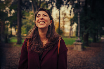 happy young woman looking at the top of the trees of a city park during autumn