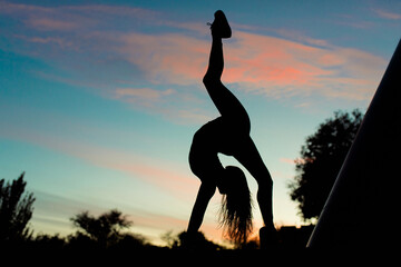 Girl acrobat at sunset doing stretching (yoga). Against the backdrop of beautiful clouds