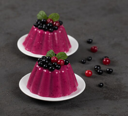 Cream jelly with black currant and cranberry on a plate on a dark background