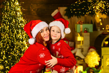 mother and son celebrate christmas. family holiday time. little boy love his mom. xmas party time. mom and kid wear santa claus hat and sweater. share presents and gifts with relatives