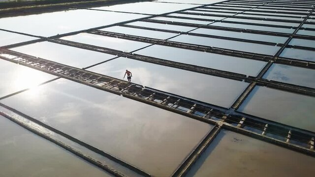 Isolated man works in salt evaporation pond, beautiful sky reflection