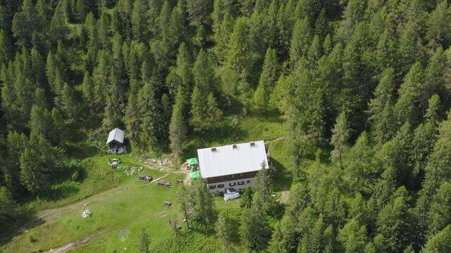 Mountain hut in the middle of Alps Peca forest. Aerial tilt up