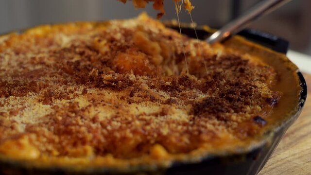 Fork dig in a cast iron skillet filled with mac and cheese, a classic American dish, baked in the oven with crispy breadcrumbs on top