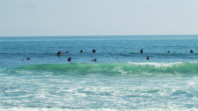 Surfers sit on there surfboards as the blue and green waves pour in
