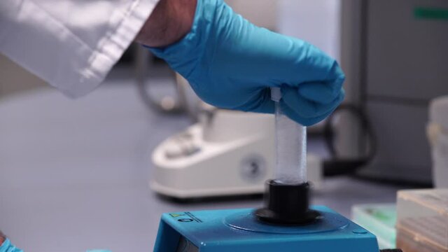 Male scientist with blue gloves mixing sample with vortex mixer. Close up