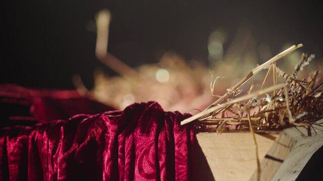 Close up focus shift of a artful decorated Christmas manger. The crip is filled with hay and a red curtain is laying on the the wooden corner