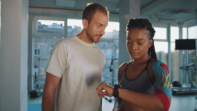 African american woman athletic and her coach trainer sport doctor standing in the gym center and looking at the sport results at fitness tracker smartwatch while prouding of personnel record