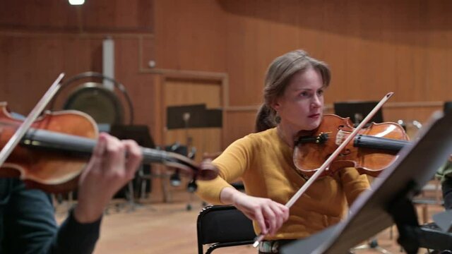 In the frame of a guy and a young woman, they play violins during a string concert, camera moves