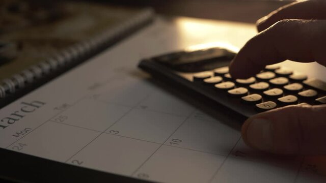 Hands using calculator on March calendar panning shot warm background