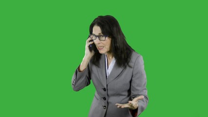 Angry mature businesswoman is shouting while talking on her cell phone. The woman is annoyed and upset she waves her arms and is furious. She is wearing a suit and glasses on green screen - Powered by Adobe