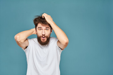 A bearded man in a white T-shirt gestures with his hands emotions blue background