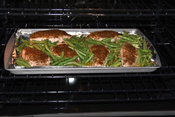 Seasoned pork chops and green beans roasting in an oven