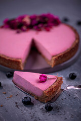 Red fruit cheesecake decorated with flowers and roses, on wooden background