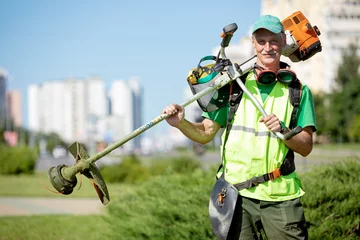 Photo sur Aluminium Couleur pistache Jardinier municipal paysagiste senior homme travailleur avec équipement de coupe-herbe à gaz sur fond de ville du soleil