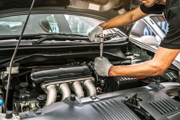 Close-up hands of auto mechanic are using the wrench to repair a car engine in auto car garage. Concepts of car care fixed repair and services.