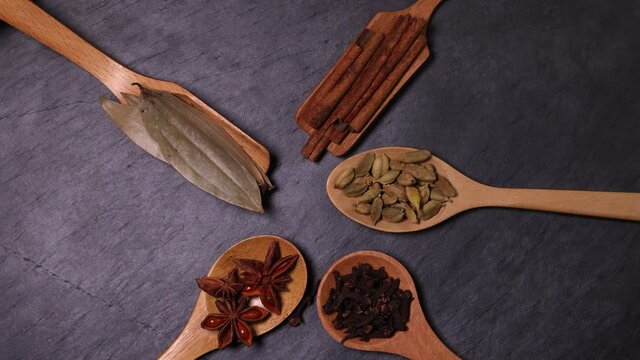 Mix variety spice cinnamon cardamom clove bay leaf wooden spoon dropping on black slate background