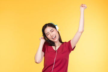 Beautiful young asian woman joyful listening to music on headphones isolated on pastel yellow wall background studio portrait.