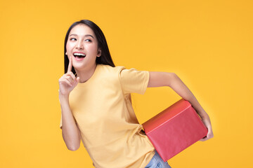 Portrait of happy smiling girl in casual holding gift box and expression face isolated over yellow background