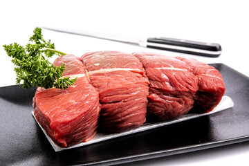 A beef sirloin tip roast with parsley garnish on a modern square black plate isolated on white
