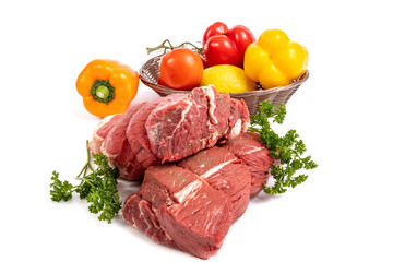 Two pieces of beef sirloin tip roast with a basket of peppers, onions, lemon and tomatoes isolated on white
