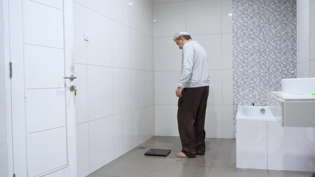 Old man measuring his weight with a scale on the morning in the bathroom at home. Shot in 4k resolution
