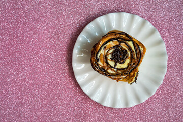 Cinnamon rolls with various sweet toppings and chocolate on a white plate on the pink glitter background.