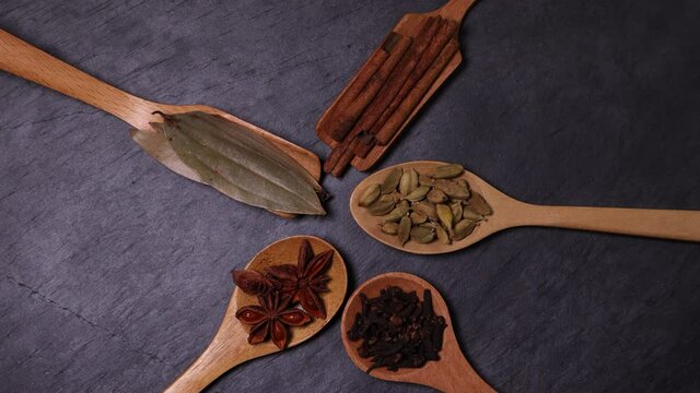 Mix variety spice cinnamon cardamom clove bay leaf wooden spoon dropping on black slate background
